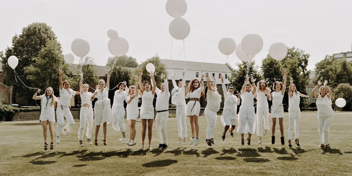 Hologic employees wearing white clothing jumping and celebrating outside with balloons